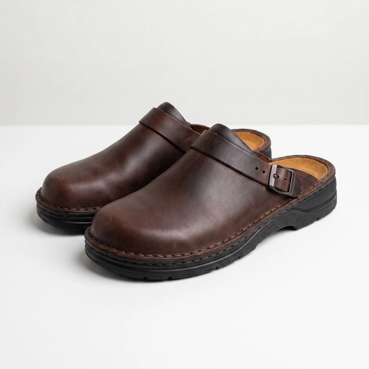 Men's closed-toe mule shoes with buckle straps and raised black soles